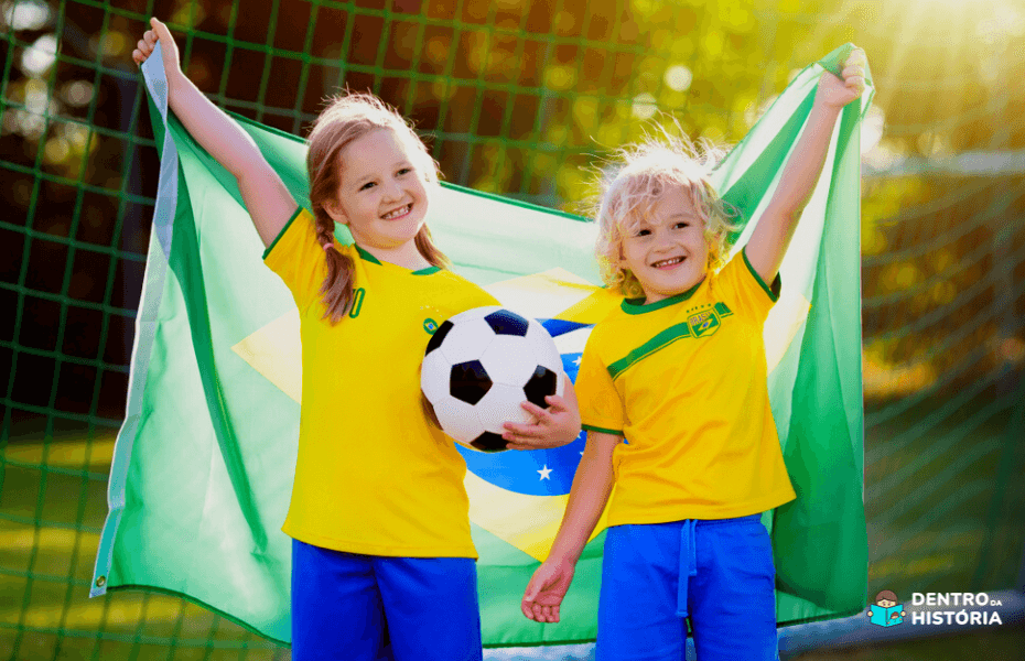 crianças segurando a bandeira do Brasil e uma bola branca e preta para torcer no Mundial de Futebol