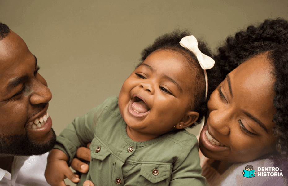 Família negra sorrindo ao segurarem sua bebê